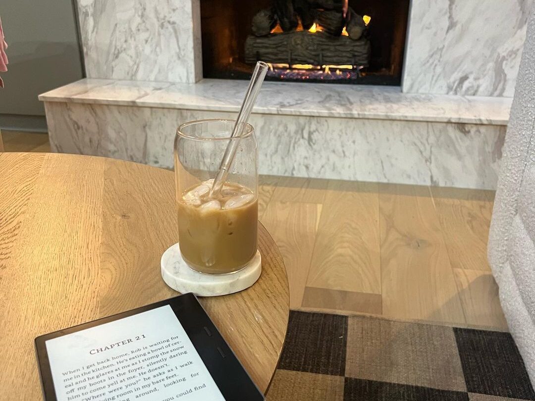 Cozy reading setup featuring fireplace, kindle, and iced coffee